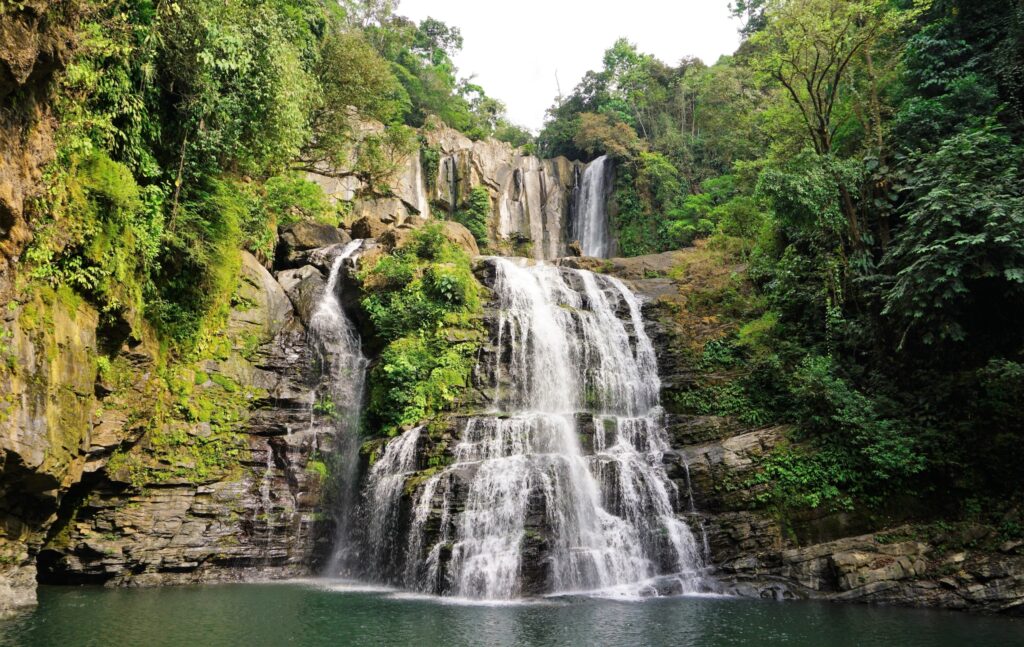 cascading waterfalls rolling down side of rocky grassy mountain into a lake