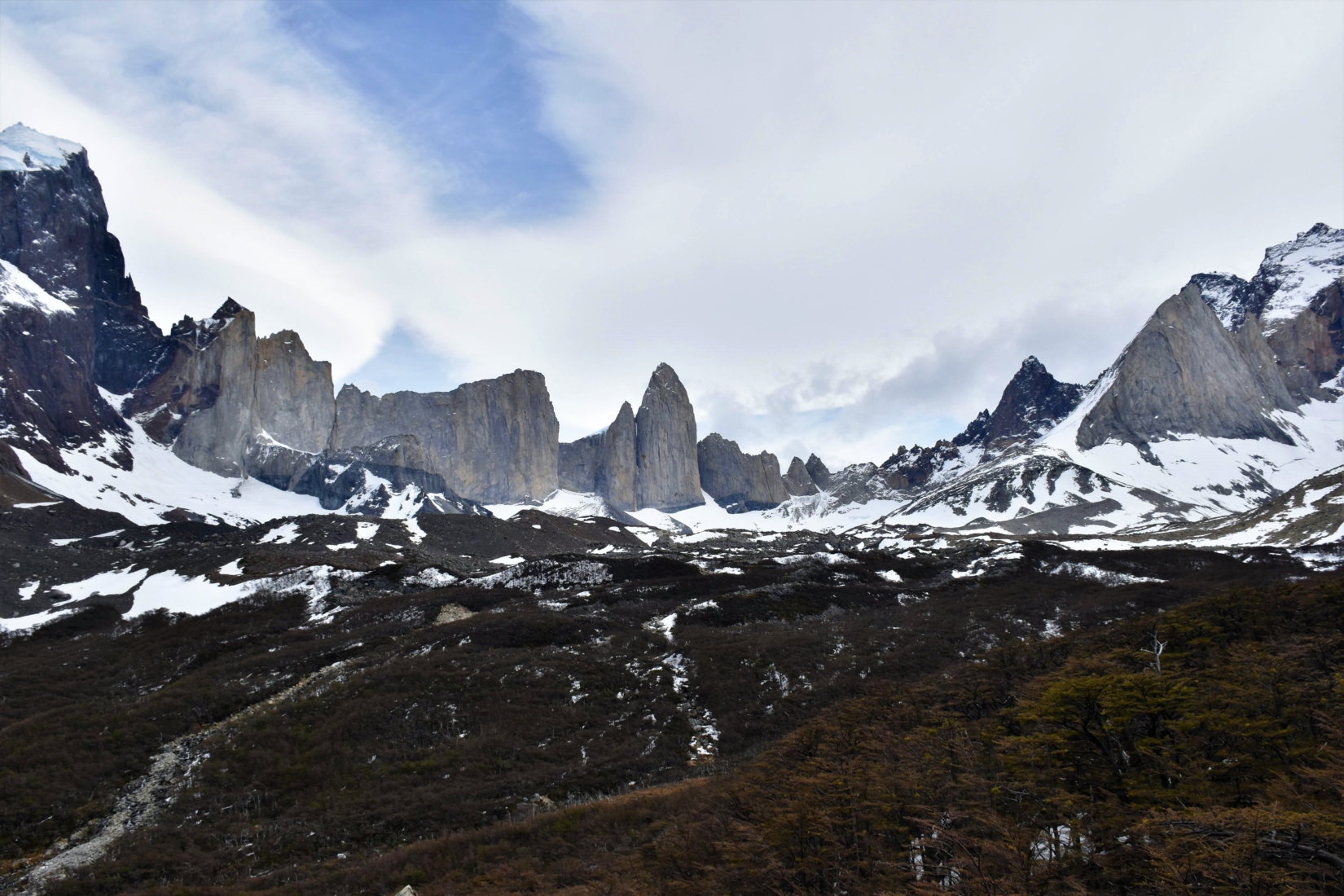 A wide mountain range with snow at the base surrounding a vast green valley in Chile.