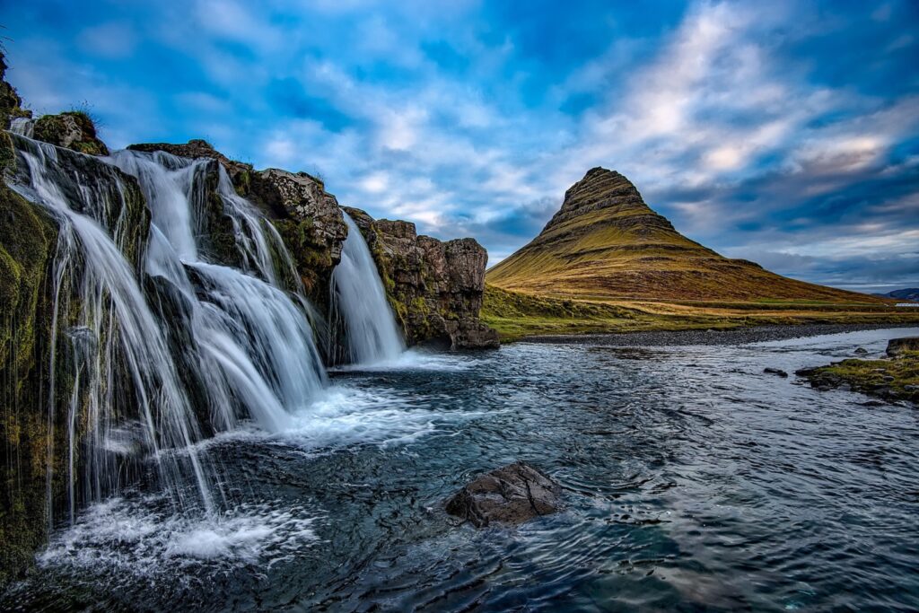 Multiple cascading waterfalls beside a cone-shaped mountain