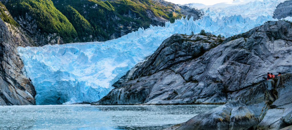 A group of people in life vests observing a large retreating glacier on a lake in Chilean Patagonia during a sustainable expedition