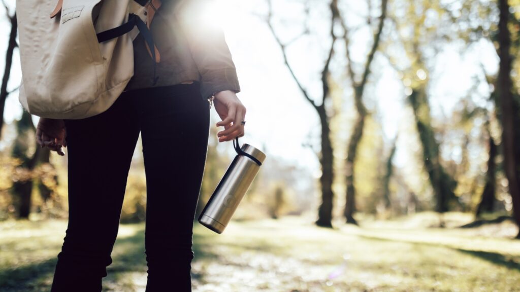 A person with a backpack traveling with a reusable water thermos bottle on a sunny day