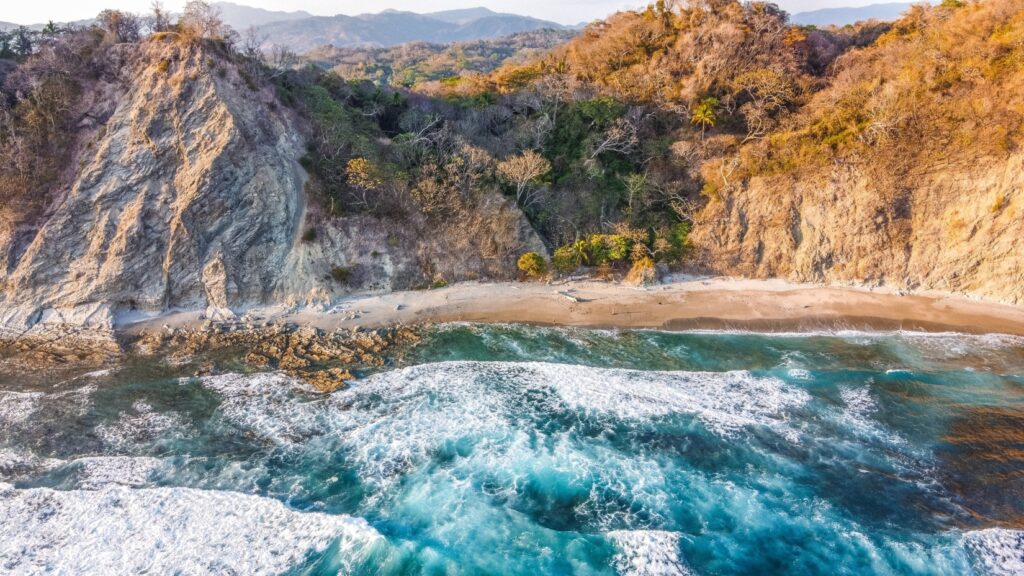 Aerial view of blue waves crashing on a beach shore surrounded by mountains