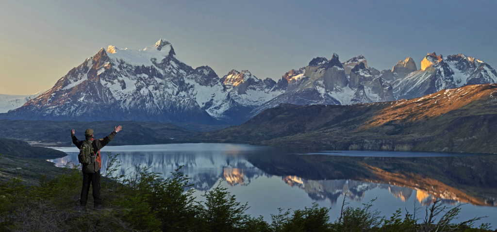 Landscape view of the mountains of Torres del Paine National Park, Chile. A man stands in the foreground with his arms outstretched in awe